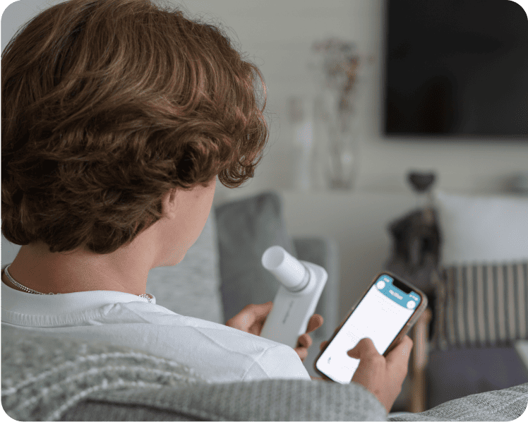 Teen in couch holding spirometer and phone